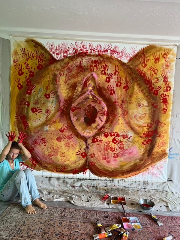 Marina Orlova seated beside large-scale handprint painting in progress